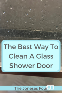 Pinterest image of the article "The Best Way to Clean a Glass Shower Door." It shows a glass shower door with water droplets on it and has the title included in the center in a blue box. The blog name "The Joneses Four" is written along the bottom.